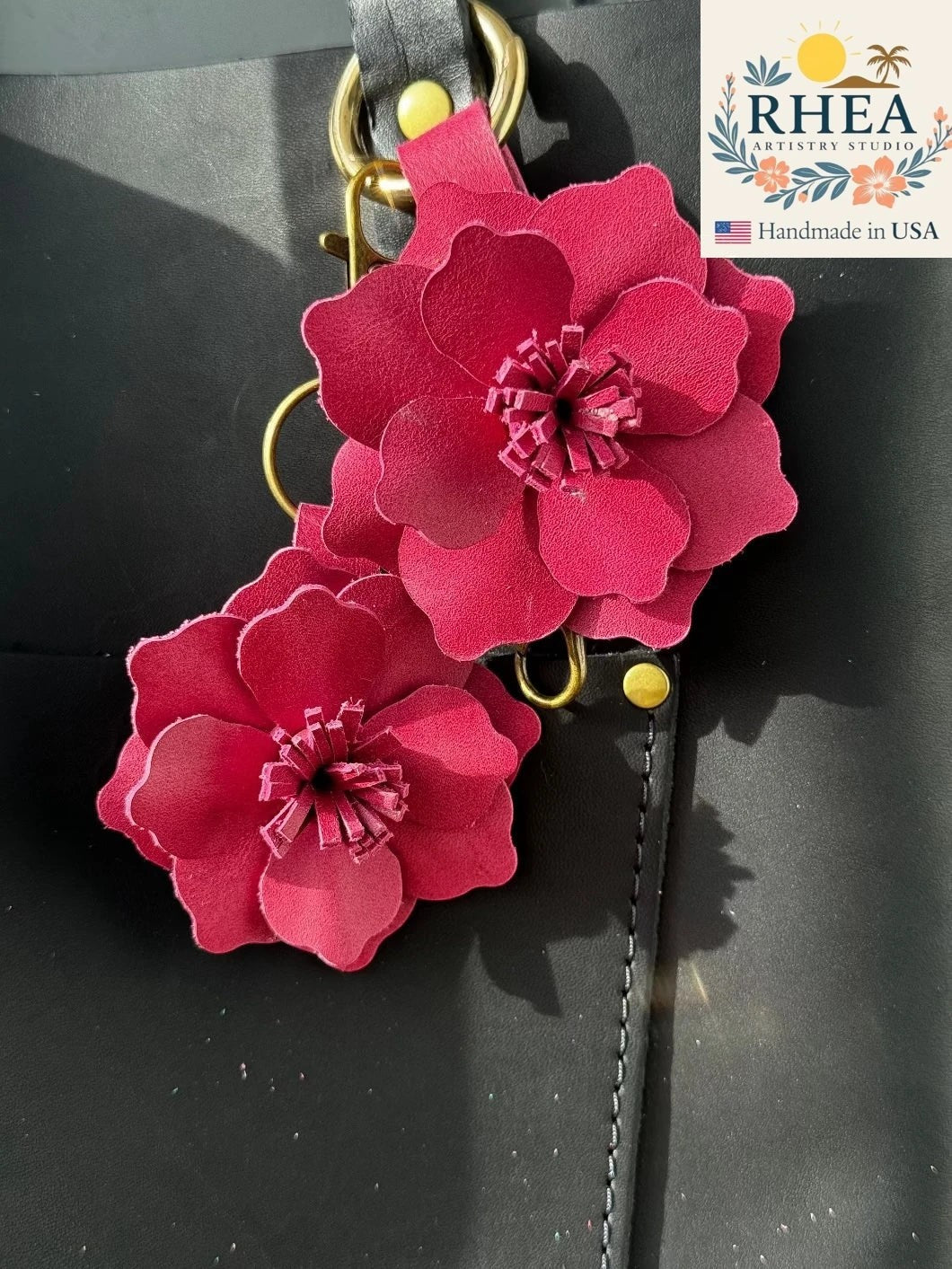Rhea Artistry Studio large old rose leather flower charm with gold lobster clasp and split ring attached to a black bag.