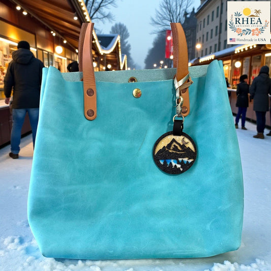 Rhea Artistry Studio hand-painted leather charm with mountain and forest silhouette, glitter front, and sunset colours. Bag accessory.