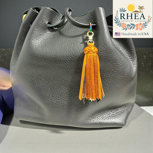 Rhea Artistry Studio handmade orange metallic leather tassel bag charm with antique brass lobster clasp.