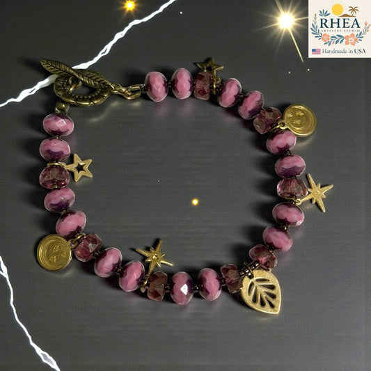 Rhea Artistry Studio pink glass bead bracelet with brass celestial charms and floral toggle clasp.