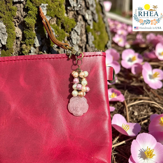 Rhea Artistry Studio handcrafted bag charm with glass pearls and a carved rose quartz pendant on a pink leather clutch.