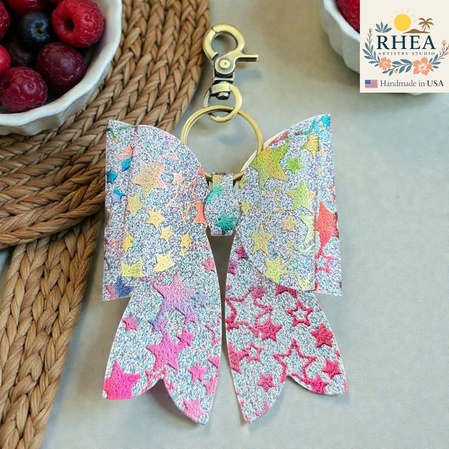 Rhea Artistry Studio handmade glittery bow bag charm with holographic stars and brass hardware.