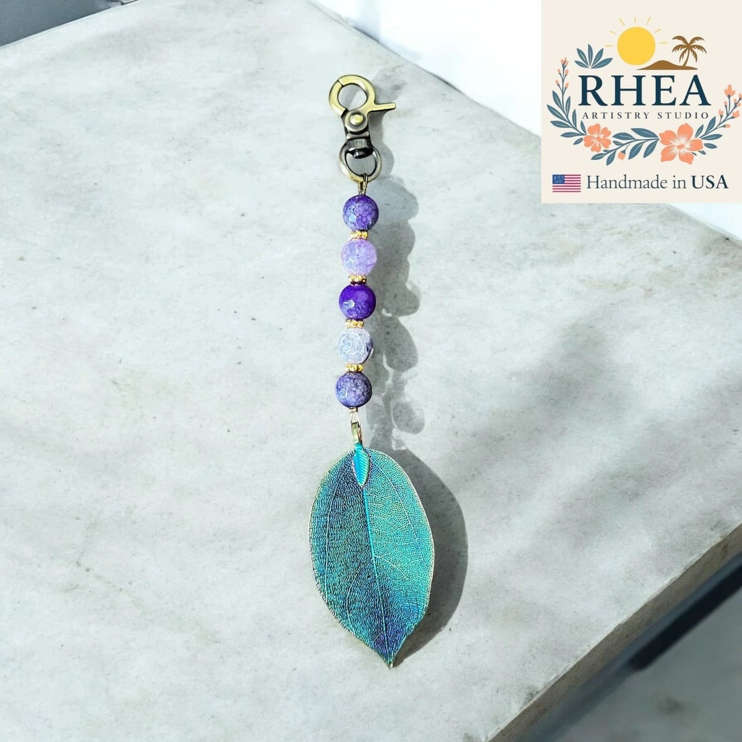 Rhea Artistry Studio handmade violet gemstone and electroplated leaf bag charm with gold clasp.