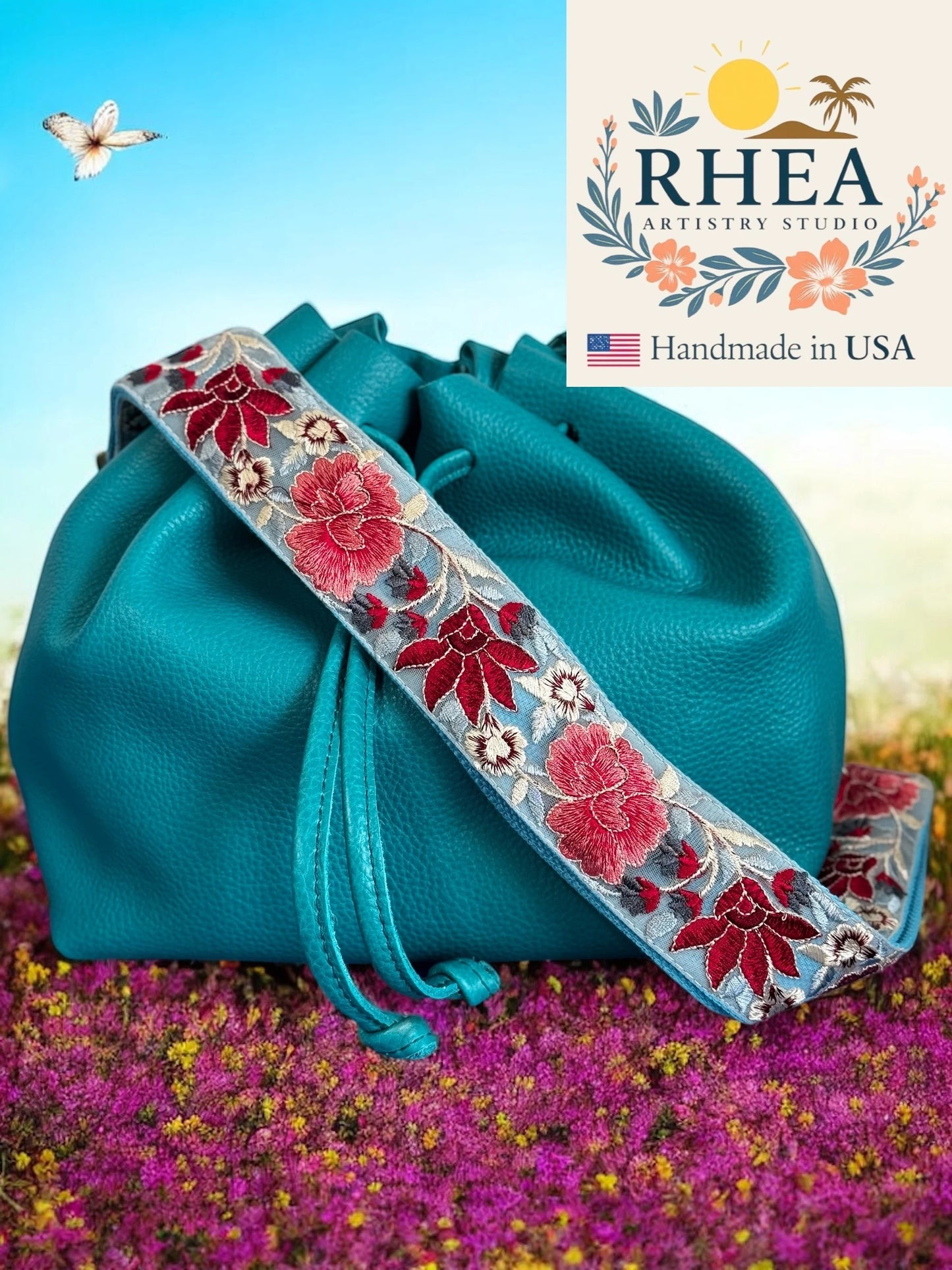 Teal handbag with floral purse strap against a scenic background, featuring RHEA Artistry Studio logo.