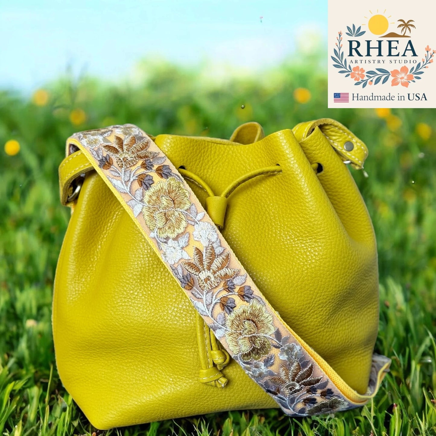 Yellow leather bag with floral purse strap on grass, RHEA brand visible