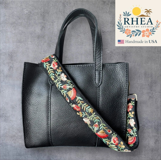 Black handbag with floral purse strap on a gray background, featuring RHEA Artistry Studio logo.