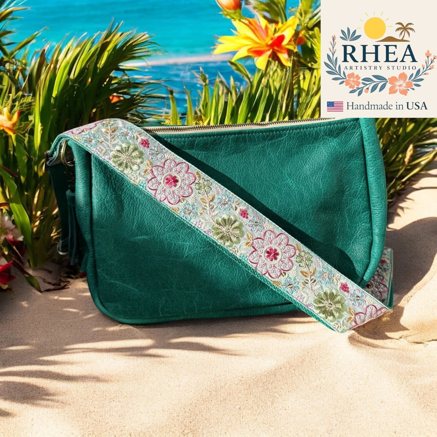 Teal clutch bag with floral purse strap on a sandy beach with RHEA Artistry Studio branding.