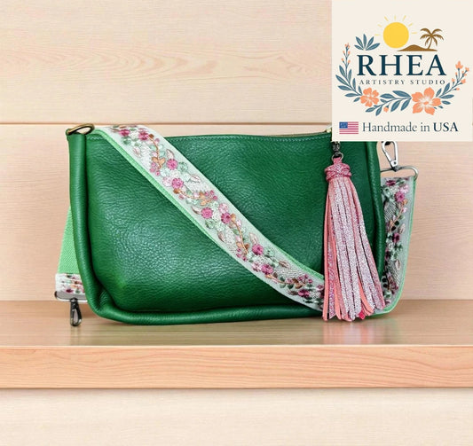 Green handbag with floral strap and tassel on a wooden surface, featuring RHEA Artistry Studio logo.