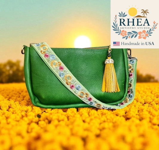 Green handbag with floral strap and tassel in a sunflower field, featuring RHEA Artistry Studio logo.