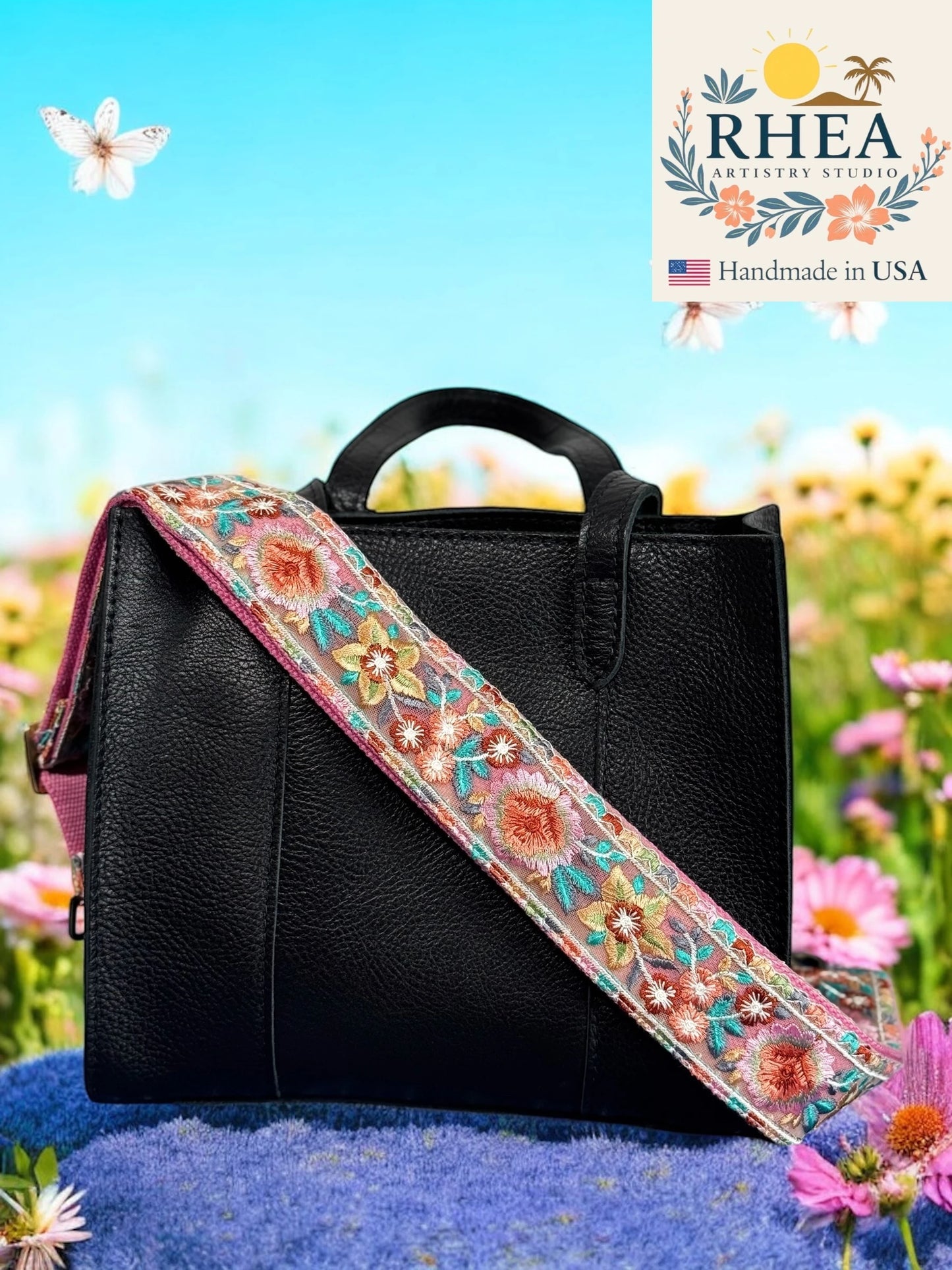 Black handbag with a colorful floral purse strap against a natural background, featuring the RHEA brand.