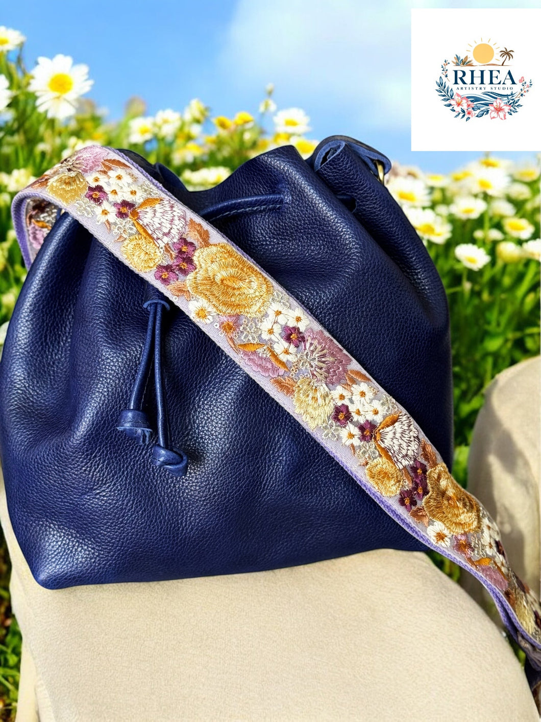 Navy blue bucket bag with lilac-embroidered wide strap featuring yellow poppies and plum accents by Rhea Artistry Studio.