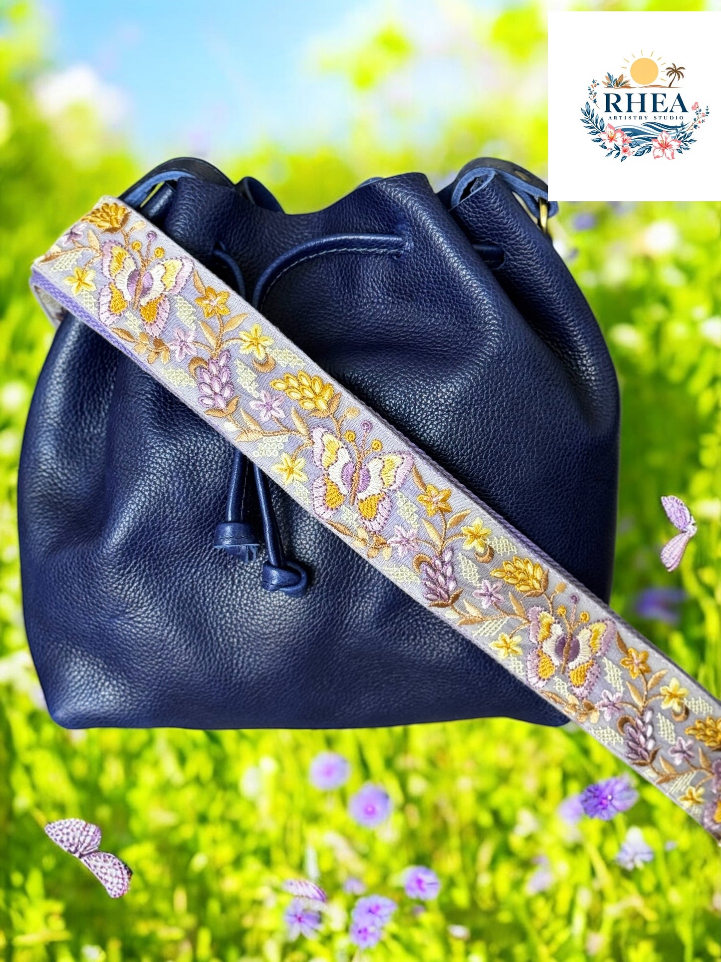 A black purse with a pink and green floral embroidered strap placed on a blue surface with flowers in the background.