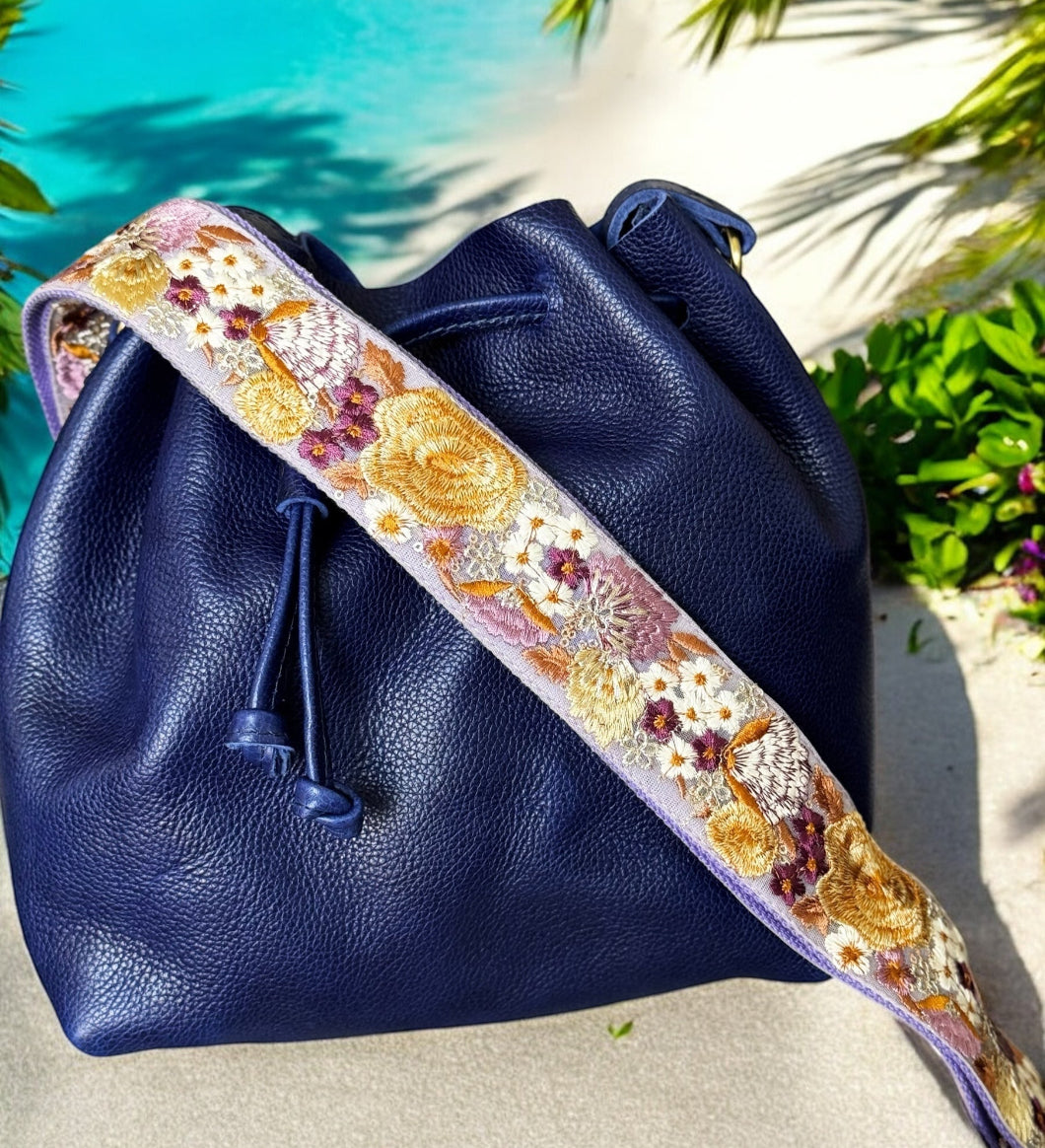 Navy blue bucket bag with lilac-embroidered wide strap featuring yellow poppies and plum accents by Rhea Artistry Studio.