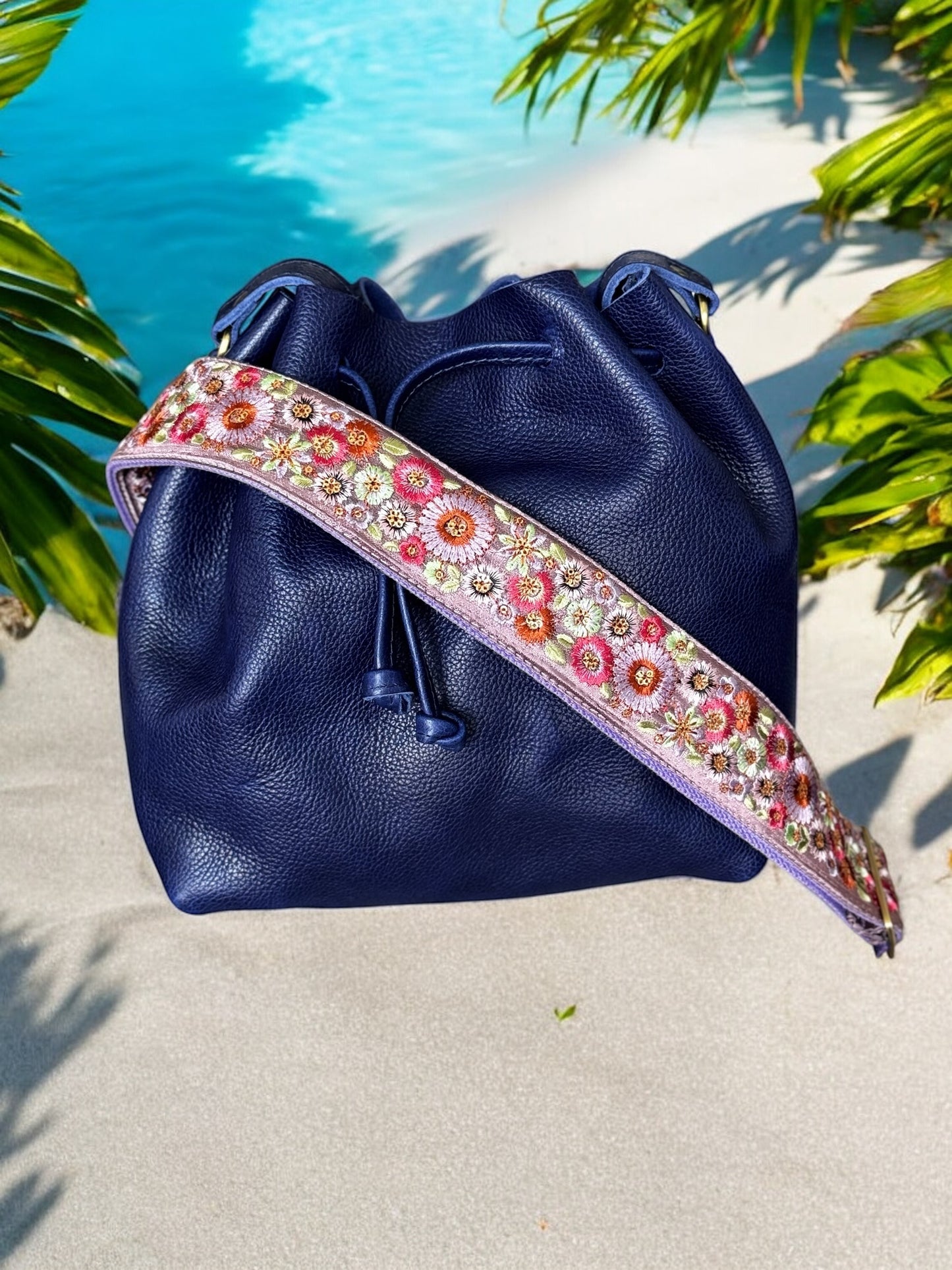 A floral embroidered purse strap in multicolor, attached to a black leather bag with brushed brass hardware.