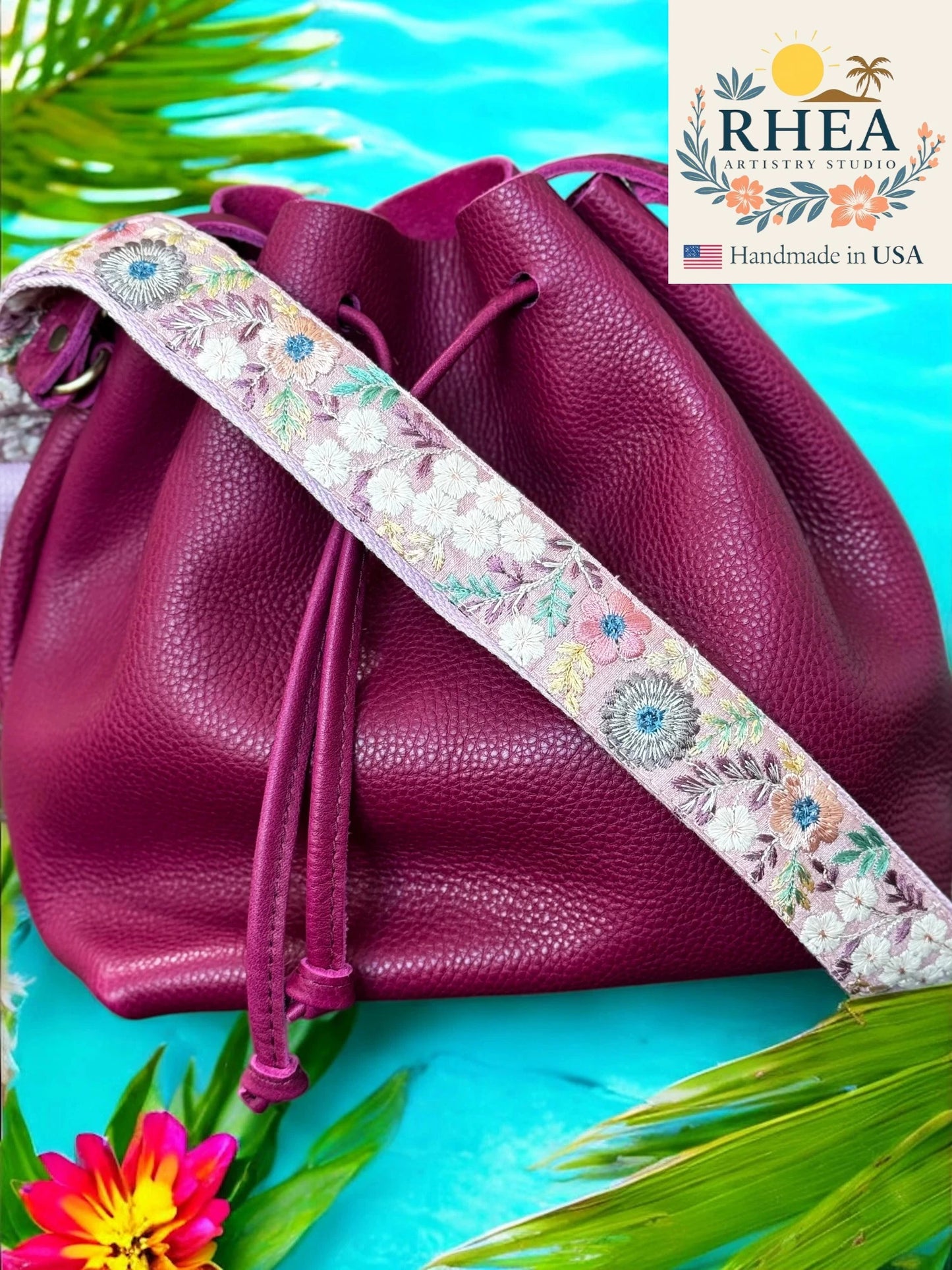 Purple leather bag with a floral strap on a blue background, featuring the RHEA brand.