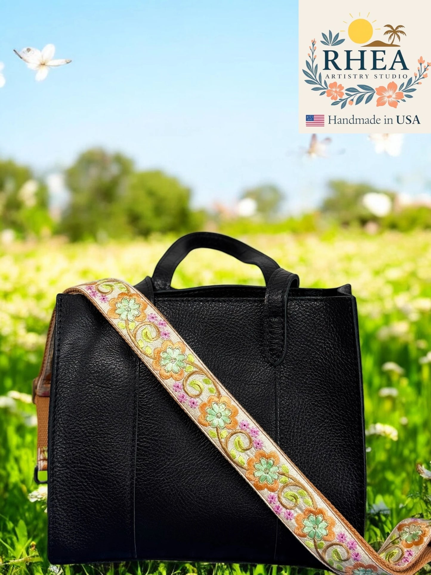 Black handbag with a colorful purse strap on grass with RHEA Artistry Studio logo.