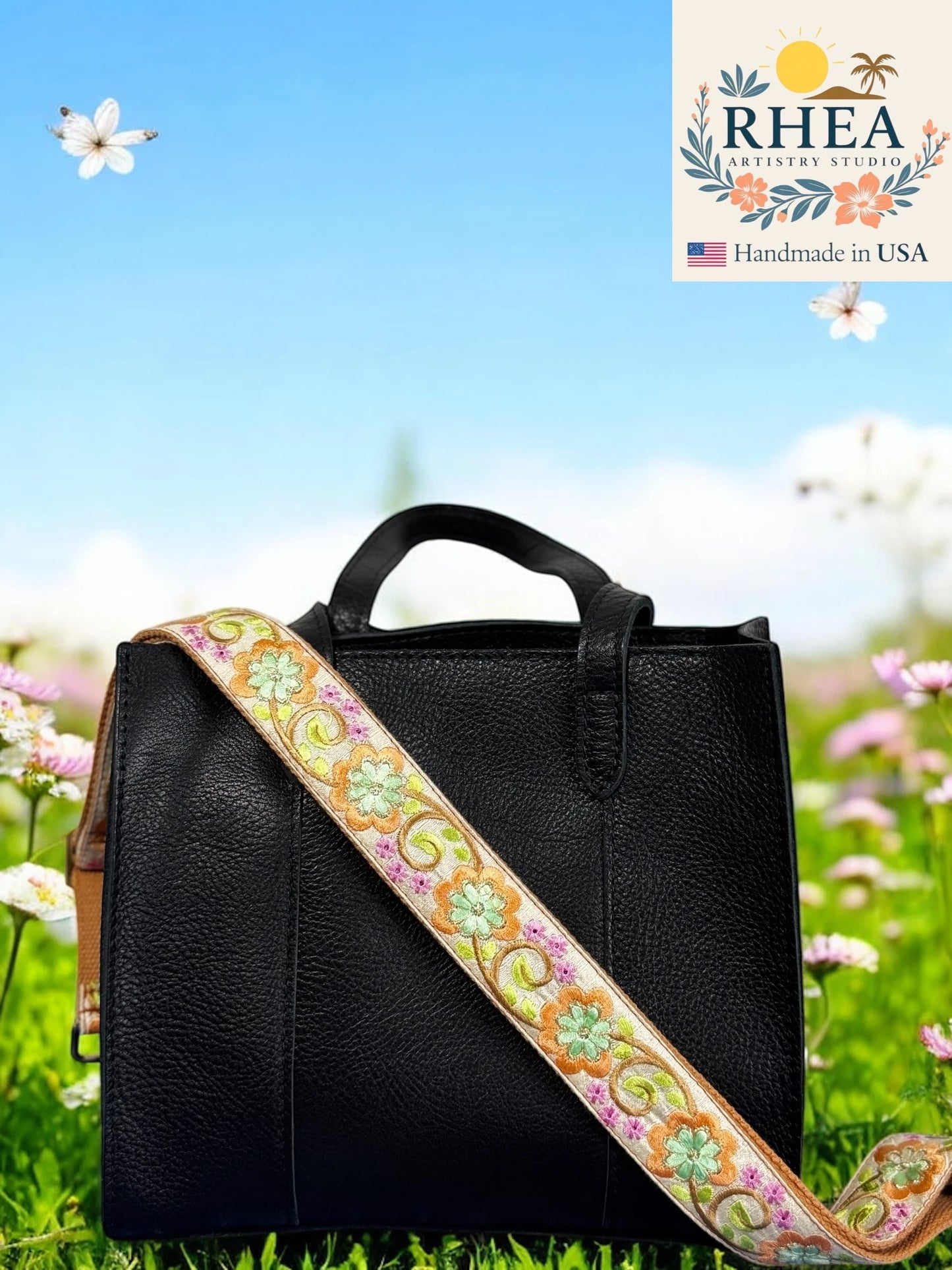 Black handbag with a colorful purse strap on grass with flowers, RHEA Artisan Studio logo visible