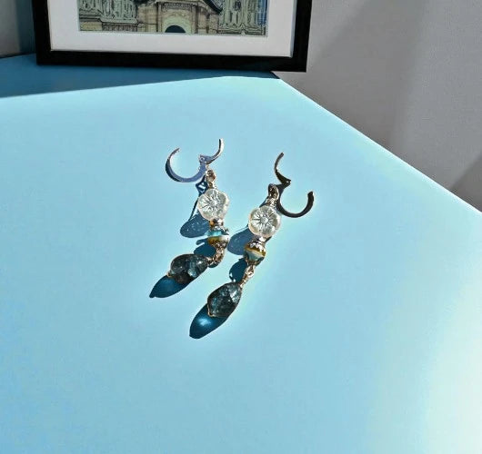 Pair of earrings with blue and clear stones on a light blue surface.