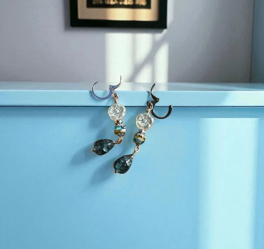 Pair of earrings with green teardrop-shaped stones on a light blue surface.