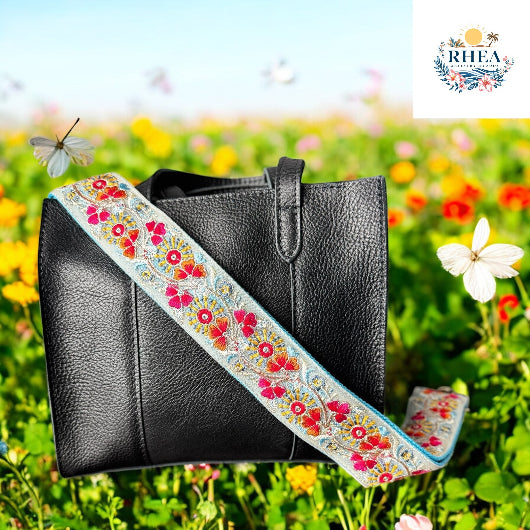 Black leather handbag with floral embroidered strap in a field of flowers.