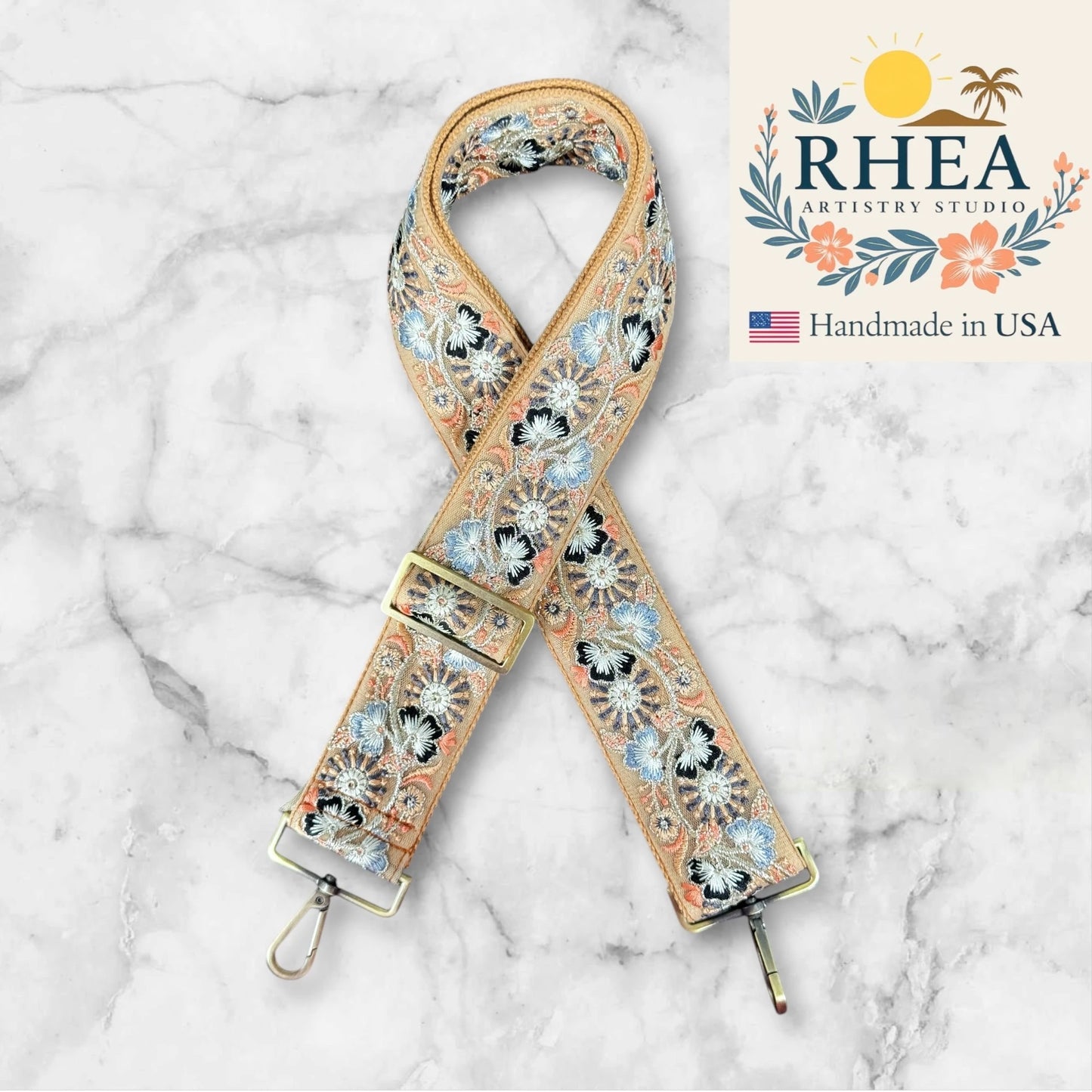 Decorative purse strap with floral pattern on a marble background, featuring the RHEA Artistry Studio logo.