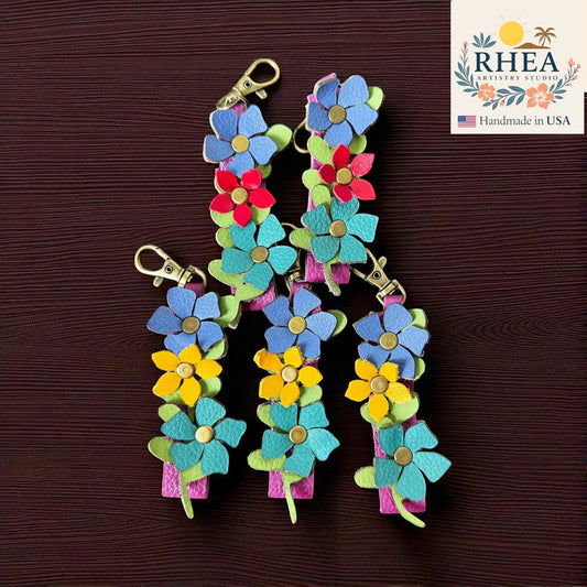Colorful flower-shaped bag charms on a brown background with RHEA branding.