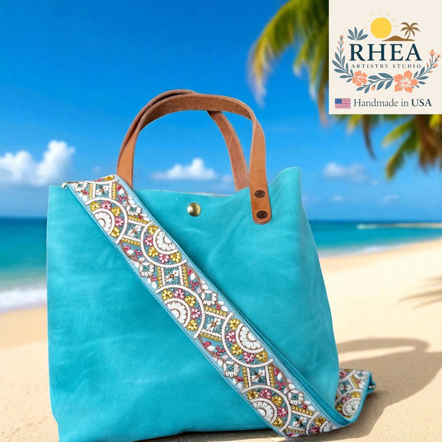 Turquoise tote bag with decorative purse strap on a beach, featuring RHEA branding.