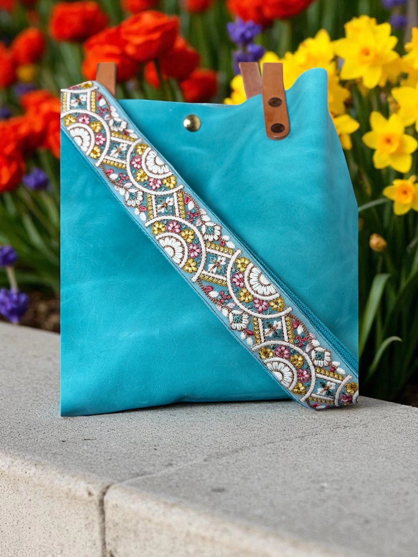 Turquoise handbag with decorative strap against a floral background