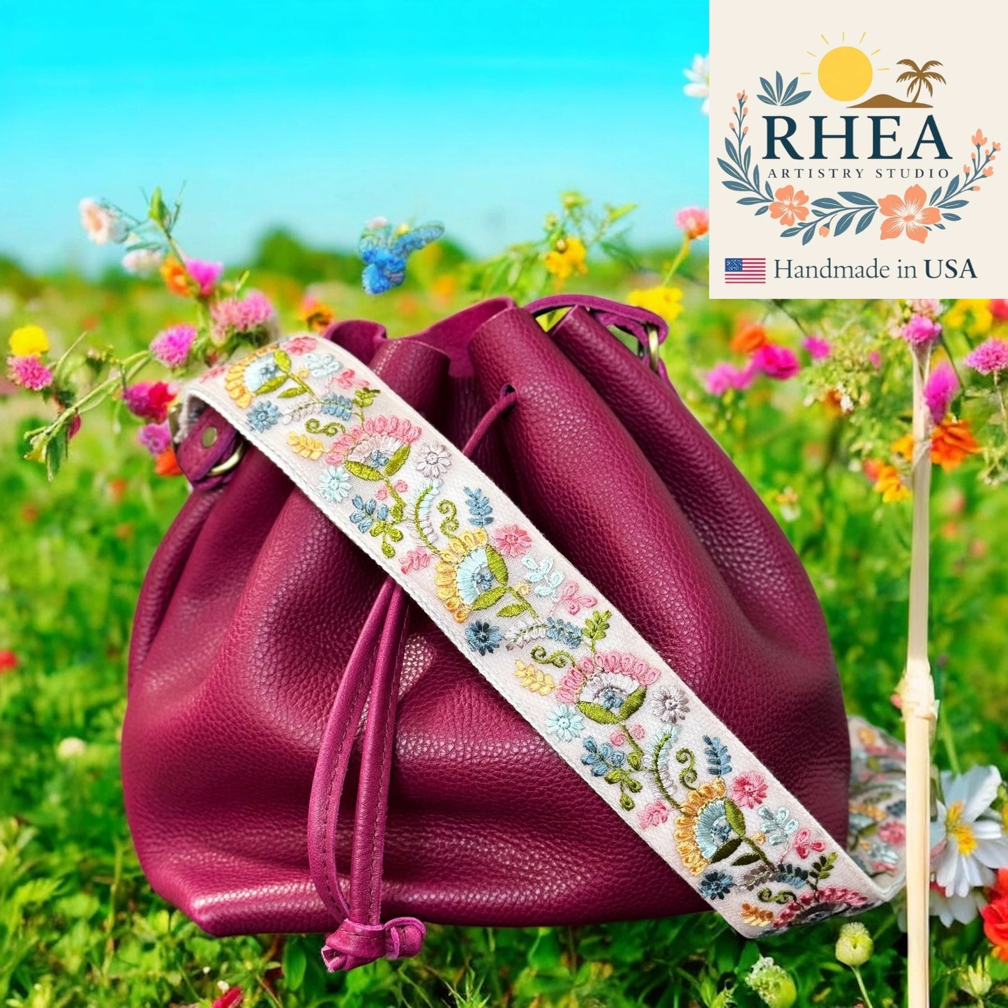 Purple drawstring bag with floral strap on a grassy field background, featuring RHEEA Artistry Studio logo.