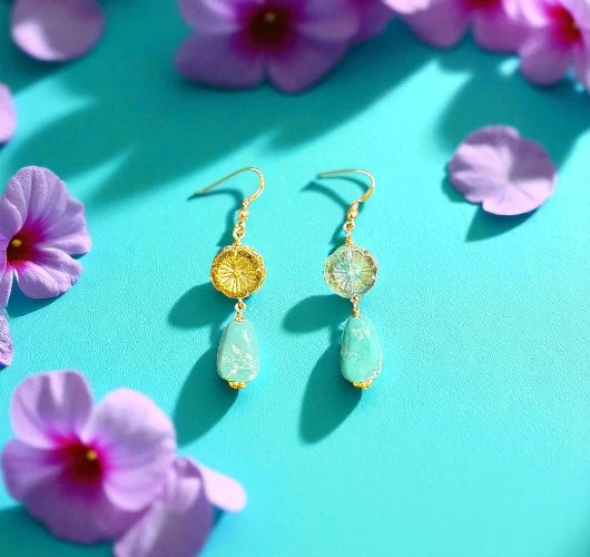 Gold and green earrings on a turquoise background with pink flowers