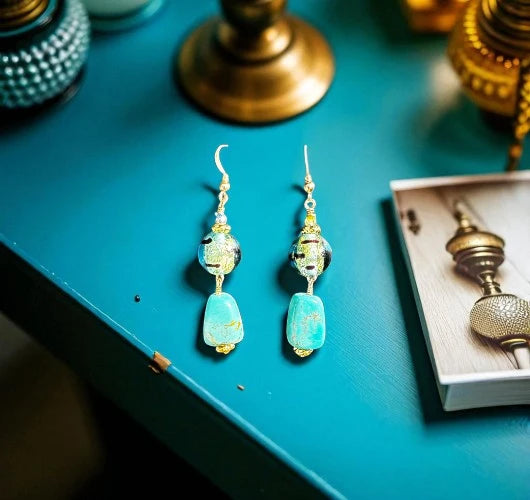Turquoise beaded earrings on a teal surface with decorative items.
