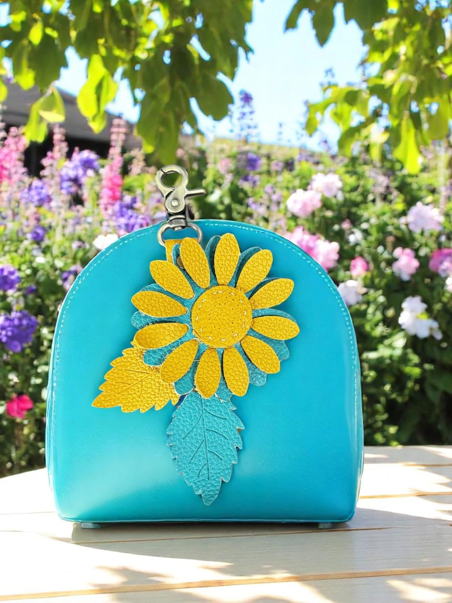 Mustard and Turquoise leather daisy charm with brushed brass clasp in a garden setting