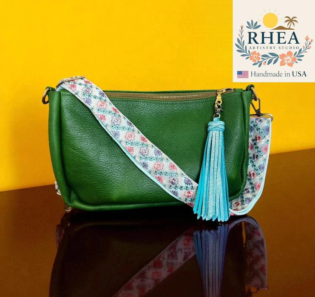 Green handbag with floral strap and tassel on a reflective surface with a yellow background, featuring the Rhea Artistry Studio logo.