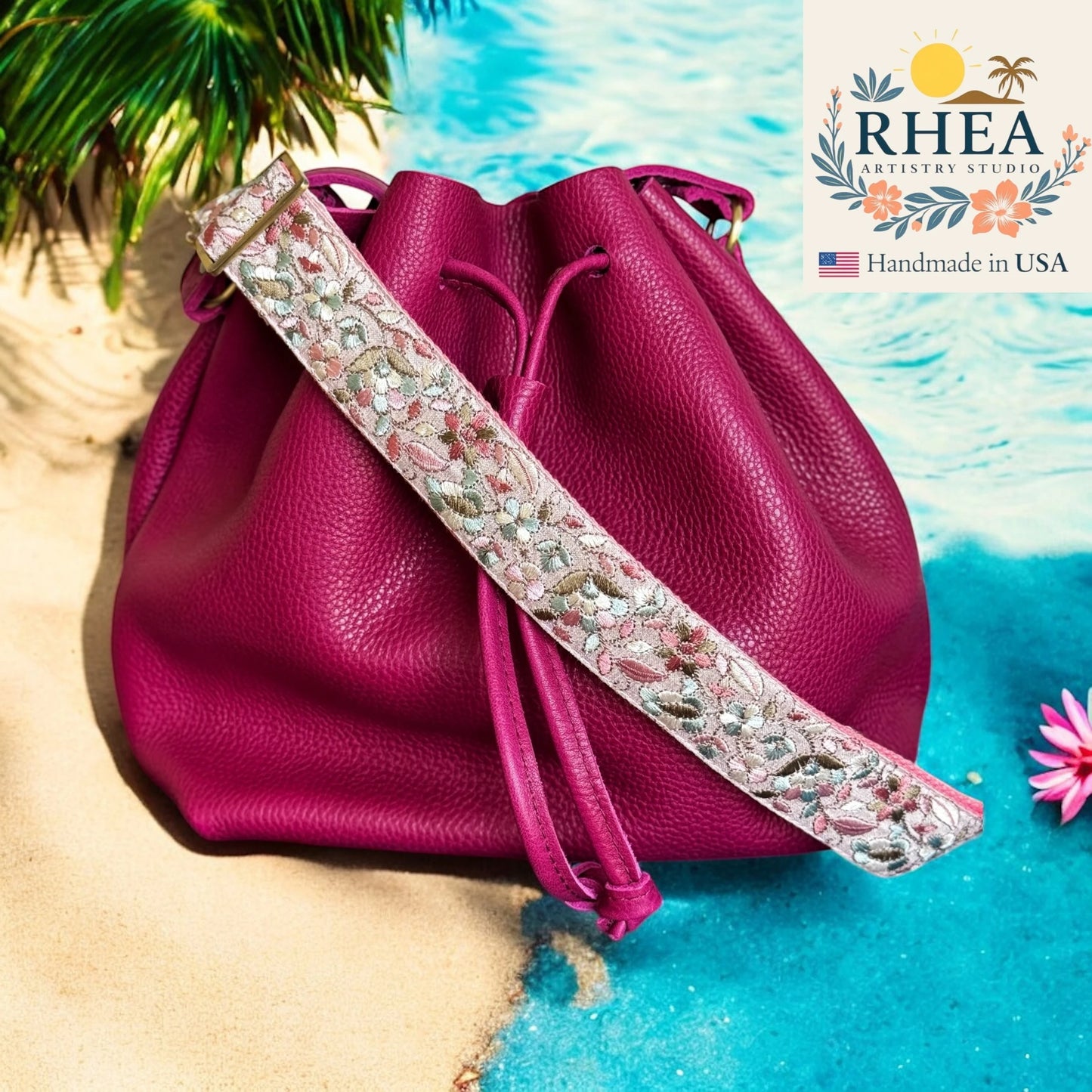 Pink leather bag with a floral purse strap on a beach background, featuring the RHEA Artistry Studio logo.
