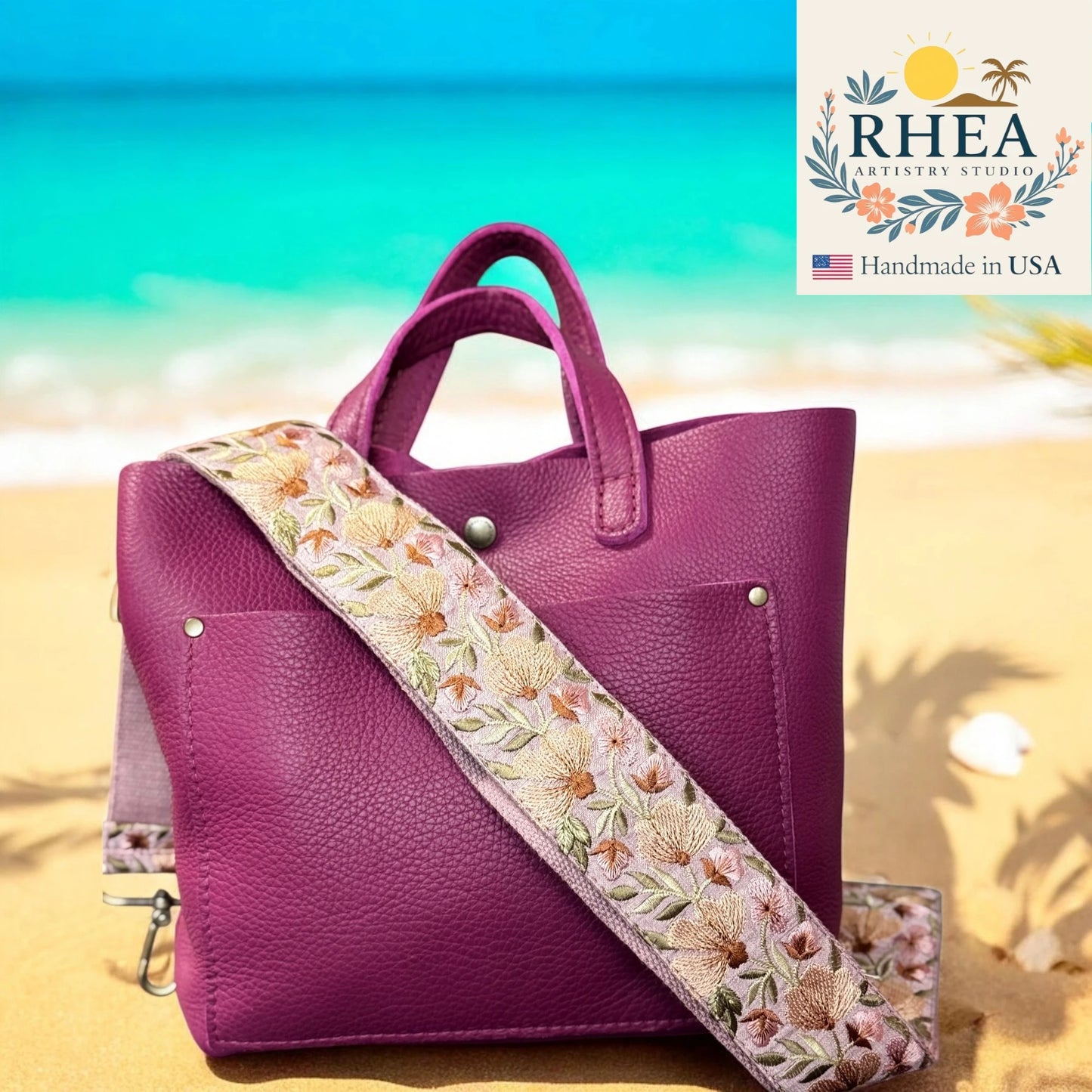 Purple handbag with floral strap on a beach, featuring the Rhea Artistry Studio logo.