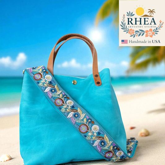 Turquoise handbag with a floral strap on a beach, featuring the RHEA Artistry Studio logo.
