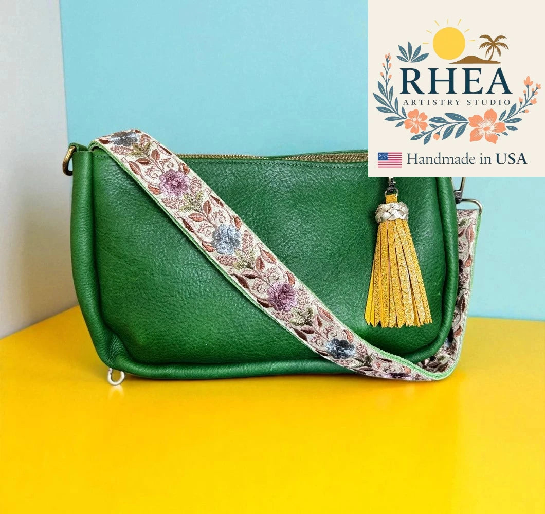 Green handbag with floral strap and tassel on a yellow surface, RHEEA Artistry Studio logo visible.