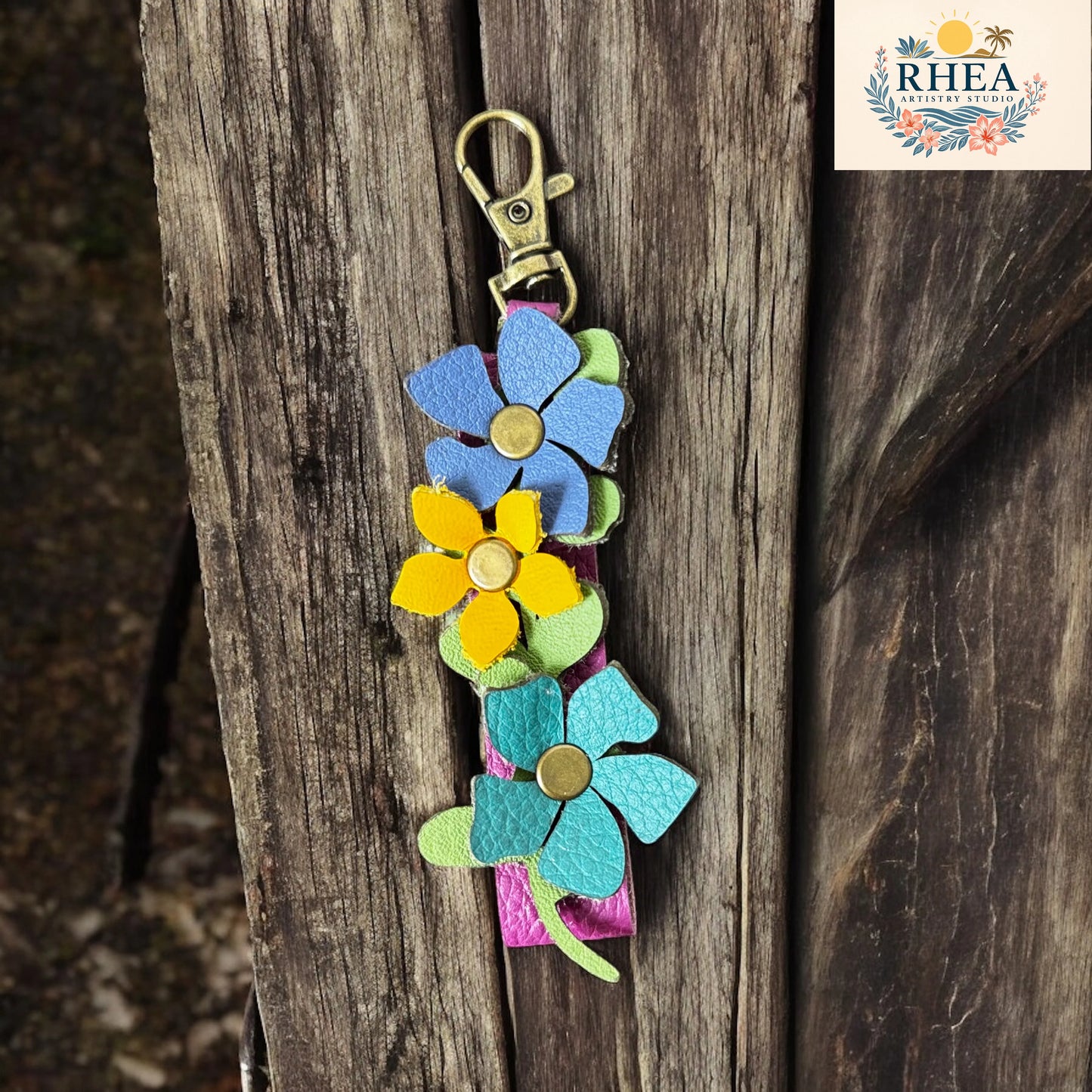 Colorful flower-shaped keychain on a wooden surface with RHEEA branding.