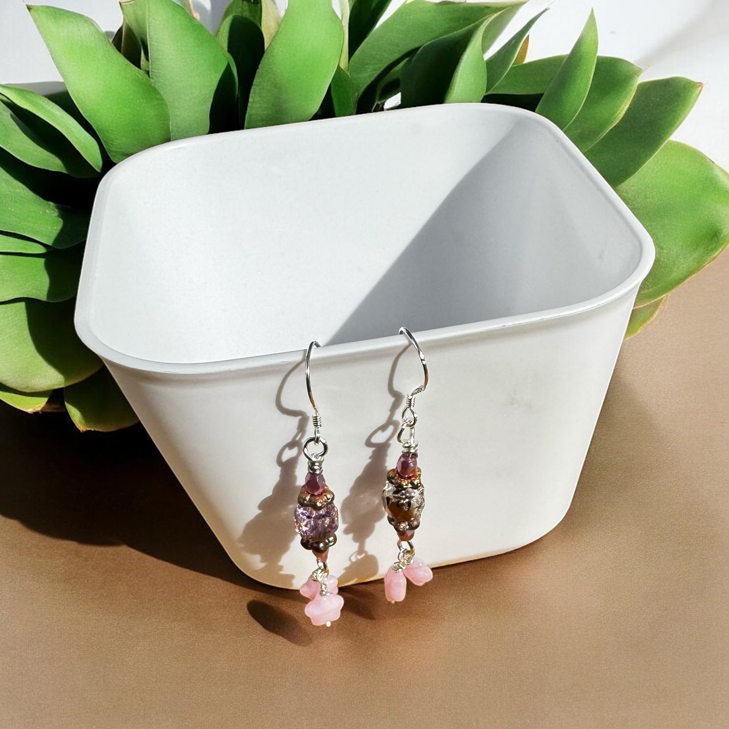 Pair of pink beaded earrings on a white dish with green leaves in the background