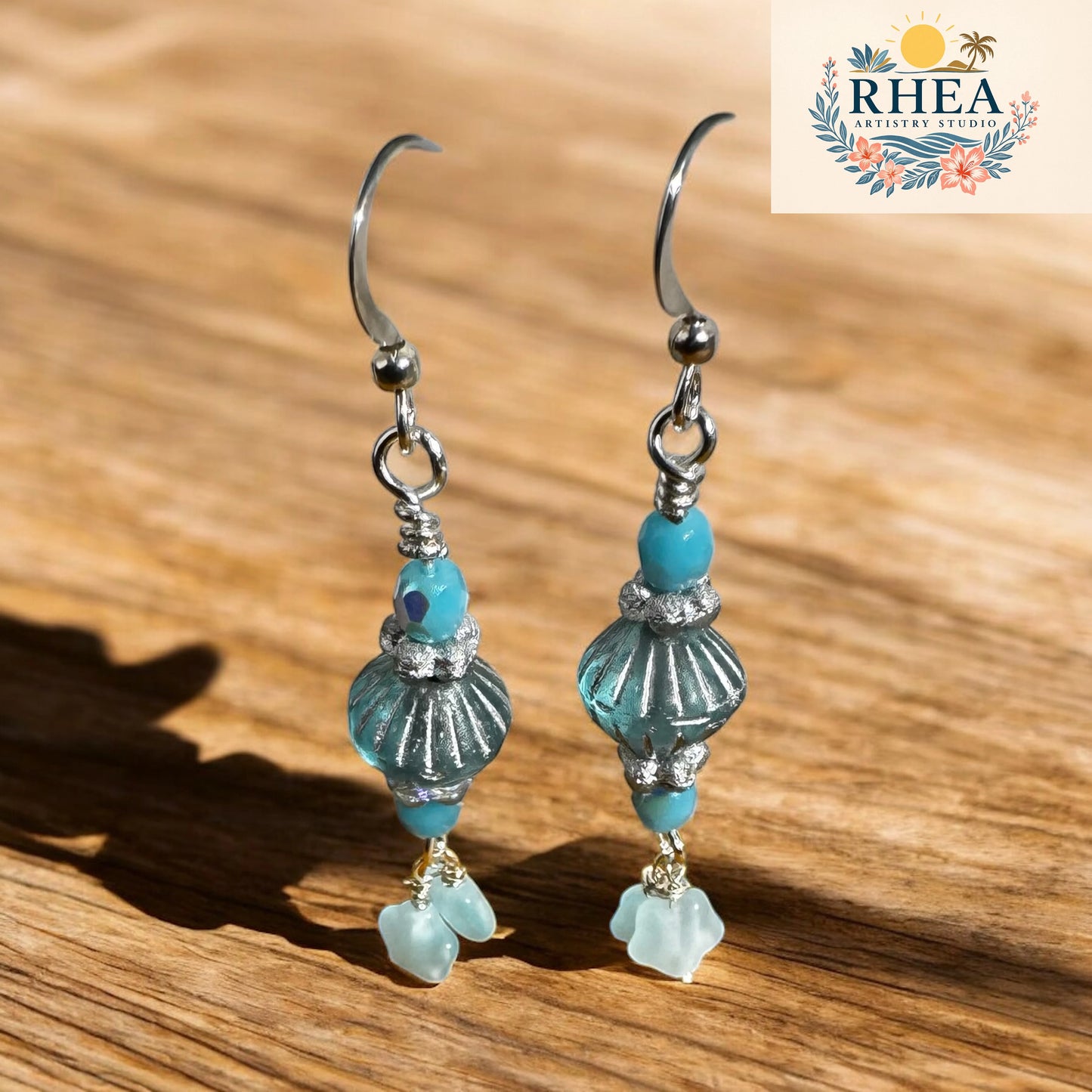 Pair of earrings with turquoise beads on a wooden surface, featuring the RHEA brand logo.
