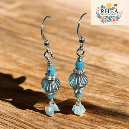 Pair of earrings with turquoise beads on a wooden surface, featuring the RHEA brand logo.