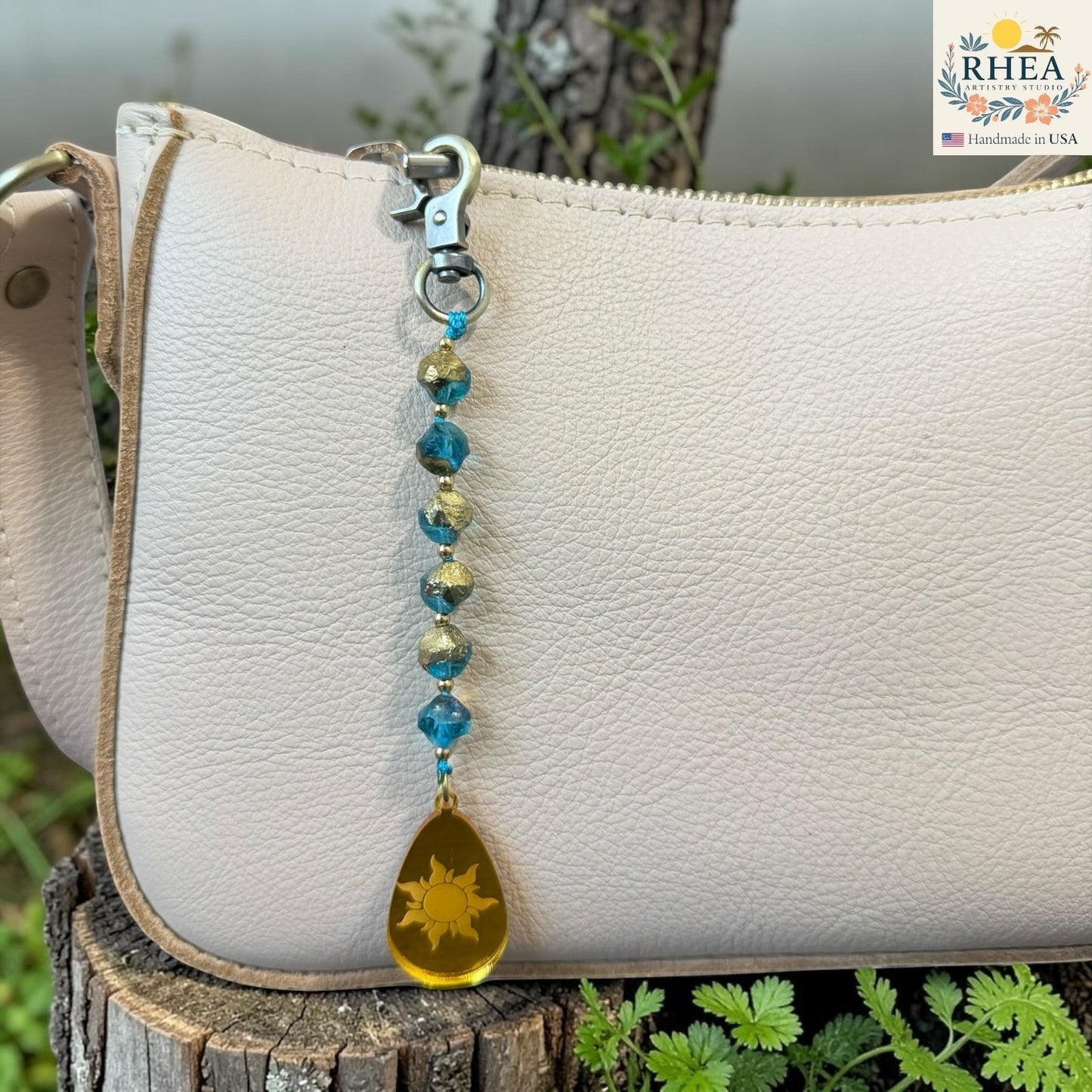 Beaded keychain with a sun charm attached to a white leather bag outdoors.