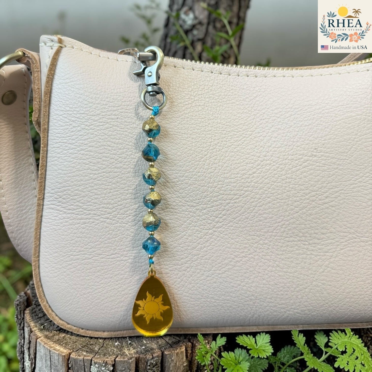 Beaded keychain with a sun charm attached to a white leather bag outdoors.