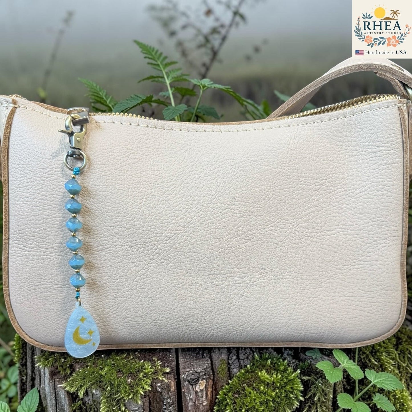 Beige handbag with a beaded keychain featuring a moon and star design, set against a natural background.