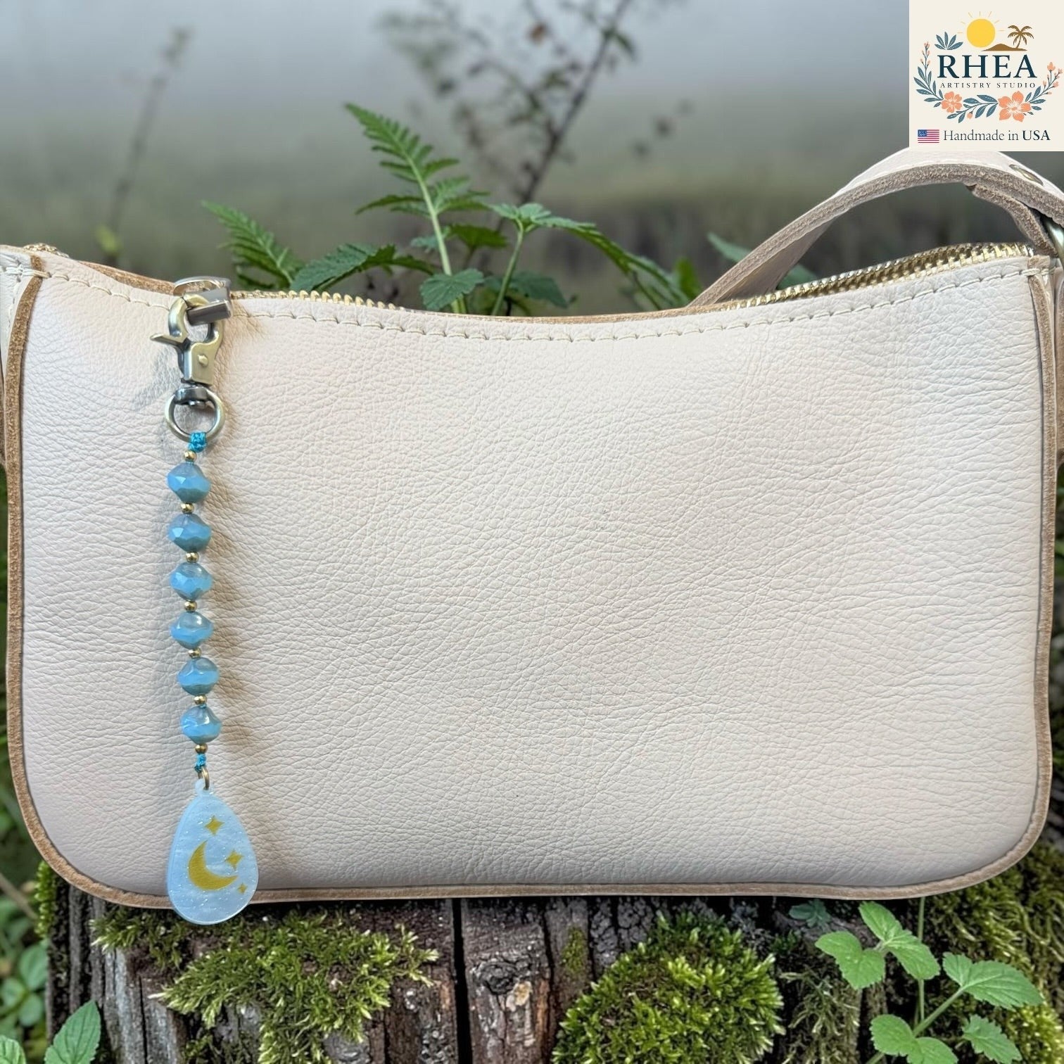 Beige handbag with a beaded keychain featuring a moon and star design, set against a natural background.