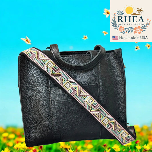 Black leather handbag with a colorful strap on a blue background, featuring the RHEA Artistry Studio logo.