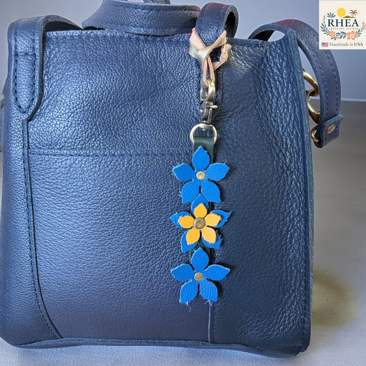 Blue leather handbag with a floral keychain charm on a neutral background