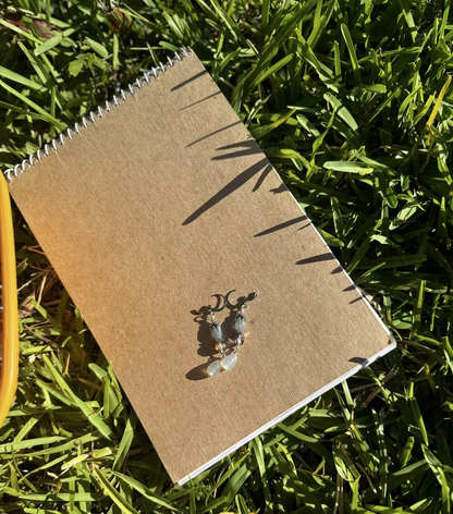 A pair of blue tulip silver earrings with a leverback closure, displayed on a brown notebook outdoors.