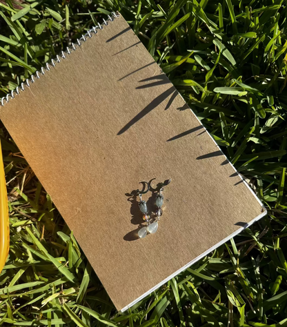 A pair of blue tulip silver earrings with a leverback closure, displayed on a brown notebook outdoors.