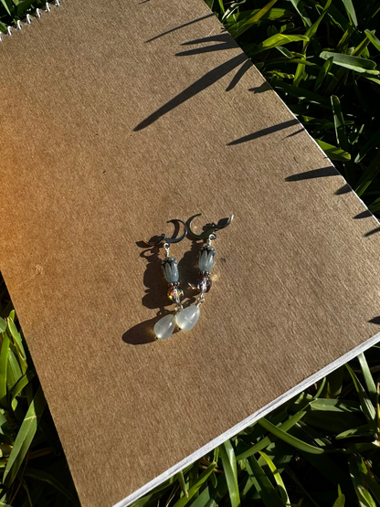 A pair of blue tulip silver earrings with a leverback closure, displayed on a brown notebook outdoors.